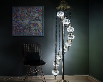 May include: A white mosaic glass floor lamp with a spiral design and multiple hanging globes. The lamp is on a dark gray background with a chair and a framed picture.