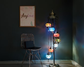 May include: A floor lamp with a metal stand and multiple colorful glass globes. The globes are decorated with intricate mosaic patterns in shades of blue, red, and orange. The lamp is lit and casting a warm glow on the surrounding area. The lamp is next to a black metal chair and a framed print with the word "Asylove" on it.