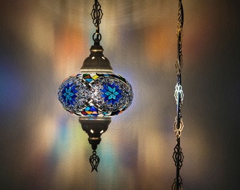 Może przedstawiać: Wisząca lampa z mozaikowego szkła w kolorze niebieskim i białym z srebrnym łańcuchem wiszącym z sufitu. Lampa jest włączona i emituje ciepłe światło.