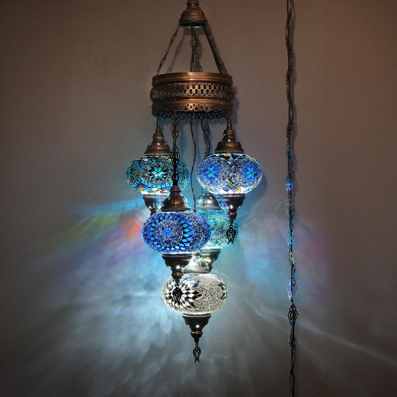 May include: A multi-tiered chandelier with five round, mosaic glass shades in shades of blue and white. The chandelier has a metal frame and is hanging from a chain.
