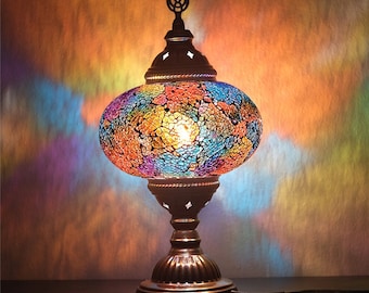 May include: A colorful mosaic glass table lamp with a round base and a decorative finial. The lamp has a warm, inviting glow.