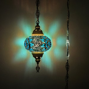 May include: A turquoise blue mosaic glass pendant light with a gold metal frame and chain. The light is on and casting a blue glow.