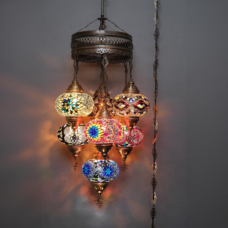 May include: A multi-tiered chandelier with six colorful mosaic glass globes. The globes are in shades of blue, green, red, yellow, and white. The chandelier has a brass finish and is suspended from a chain.
