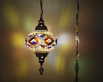 May include: A colorful mosaic glass pendant light with a gold chain hanging from the ceiling. The light is on and casting a warm glow.