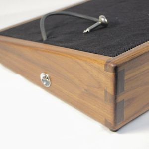 May include: A wooden pedalboard with a black felt surface and a cable with a metal jack. The pedalboard is made of dark wood with dovetail joints and a silver input jack.