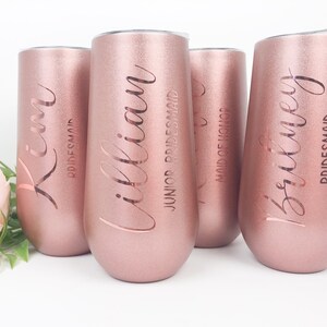 May include: Set of five rose gold stainless steel tumblers with engraved names and titles, including "Kim, Bridesmaid", "illian, Junior Bridesmaid", "Maid of Honor", "Britney, Bridesmaid".