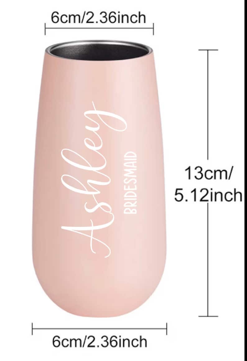 May include: A pink stainless steel champagne flute with the name "Ashley" and the word "Bridesmaid" in white lettering. The flute is 5.12 inches tall and 2.36 inches wide.