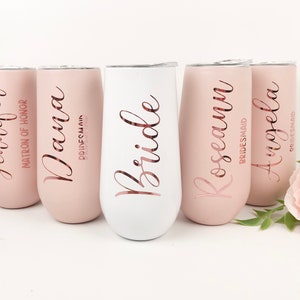 May include: Five stainless steel tumblers with personalized names and titles, including "Bride", "Matron of Honor", and "Bridesmaid". The tumblers are in shades of pink and white.