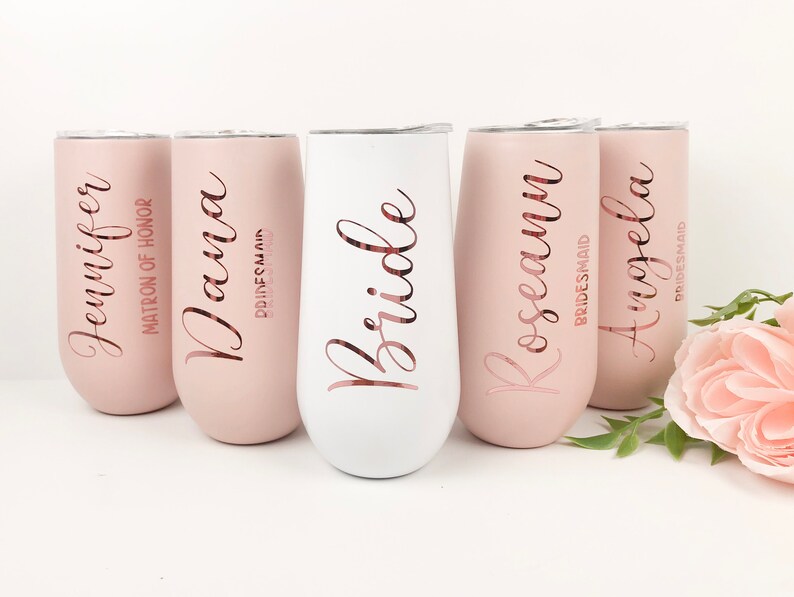 May include: Five stainless steel tumblers with personalized names and titles, including "Bride", "Matron of Honor", and "Bridesmaid". The tumblers are in shades of pink and white.