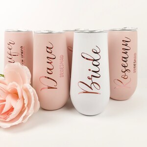 May include: Set of five stainless steel champagne flutes with rose gold lettering. The flutes are in two colors: pink and white. The text on the flutes reads "Bride", "Wife", "Nana Bridesmaid", "Roseann Bridesmaid".
