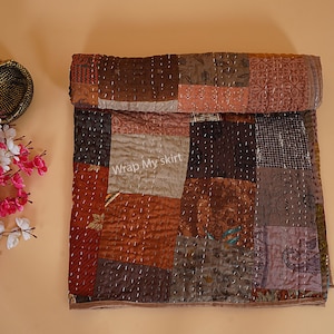 Könnte beinhalten: Eine braune und beige Patchwork-Decke mit verschiedenen Mustern und Texturen. Die Decke ist in der Hälfte gefaltet und hat ein Etikett mit der Aufschrift "Wrap My Skirt".