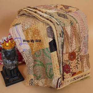 Könnte beinhalten: Ein Patchwork-Quilt mit verschiedenen Mustern und Farben, darunter Beige, Braun und florale Designs. Der Quilt hat sichtbare Nähte und den Text "Wrap My Skirt". Eine dekorative Löwenstatue mit goldener Krone befindet sich im Hintergrund.