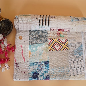 May include: A white kantha quilt with a patchwork design featuring various patterns and colors, including blue, red, and yellow. The quilt is made of recycled saris and is hand-stitched. "Wrap My Skirt" is written on the quilt.