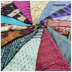 May include: A collection of colourful kantha quilts arranged in a circular pattern. The quilts are made from recycled saris and feature various floral and geometric designs. The quilts are a vibrant mix of colours, including blue, pink, purple, green, and brown.