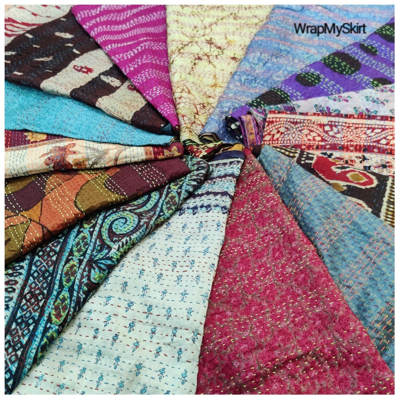 May include: A collection of colourful kantha quilts arranged in a circular pattern. The quilts are made from recycled saris and feature various floral and geometric designs. The quilts are a vibrant mix of colours, including blue, pink, purple, green, and brown.