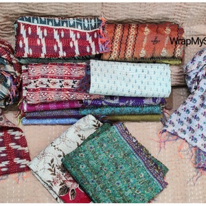 May include: A collection of colorful silk scarves with various patterns and designs. The scarves are made of kantha fabric, a traditional Indian hand-stitched fabric. The scarves are arranged in a pile on a beige surface. The text "WrapMySkirt" is visible in the upper right corner of the image.
