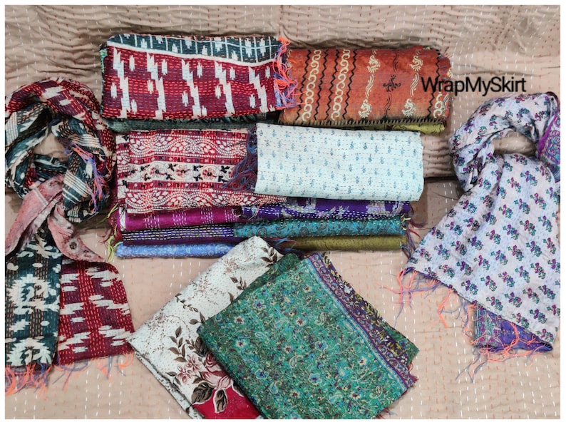May include: A collection of colorful silk scarves with various patterns and designs. The scarves are made of kantha fabric, a traditional Indian hand-stitched fabric. The scarves are arranged in a pile on a beige surface. The text "WrapMySkirt" is visible in the upper right corner of the image.