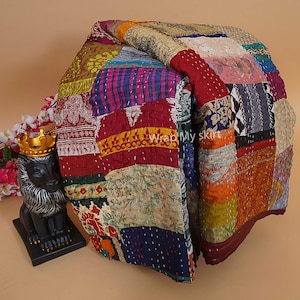 Puede incluir: Una colcha de retazos colorida hecha de saris reciclados. La colcha est&aacute; hecha de cuadrados de diferentes telas, colores y patrones. La colcha est&aacute; doblada por la mitad y est&aacute; sobre una superficie marr&oacute;n claro.