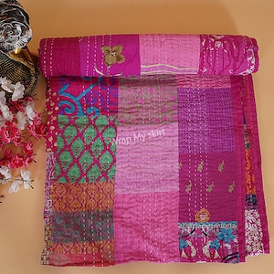 May include: A pink kantha quilt with a patchwork design featuring various floral and geometric patterns. The quilt is made of recycled saris and is hand-stitched.
