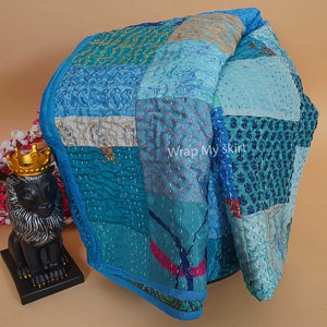 Pu&ograve; includere: Un trapunta patchwork blu e turchese con una variet&agrave; di motivi floreali e geometrici. La trapunta &egrave; realizzata in seta ed &egrave; cucita a mano. La trapunta &egrave; piegata a met&agrave; e si trova su una superficie marrone chiaro.