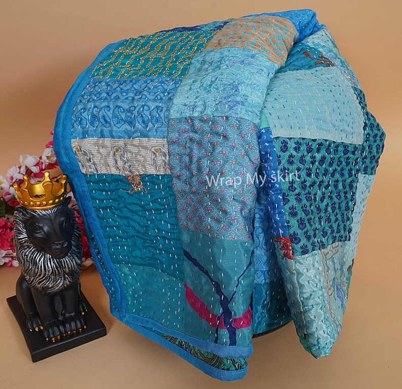 Pu&ograve; includere: Un trapunta patchwork blu e turchese con una variet&agrave; di motivi floreali e geometrici. La trapunta &egrave; realizzata in seta ed &egrave; cucita a mano. La trapunta &egrave; piegata a met&agrave; e si trova su una superficie marrone chiaro.