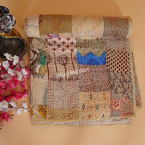 Könnte beinhalten: Eine Patchwork-Decke mit verschiedenen braunen, beige und blauen Mustern. Die Decke besteht aus verschiedenen Stoffen, die in einem zufälligen Muster zusammengenäht sind. Die Decke ist in der Hälfte gefaltet und liegt auf einer hellbraunen Oberfläche.