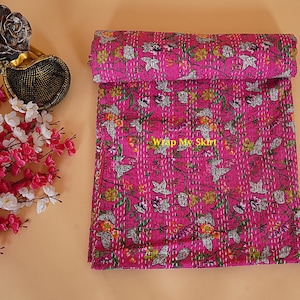 Könnte beinhalten: Eine aufgerollte magentafarbene Steppdecke mit einem Blumenmuster mit grünen Blättern und orangefarbenen und gelben Blüten. Die Steppdecke ist mit weißem Faden bestickt. Der Text "Wrap My Skirt" ist auf der Steppdecke zu sehen.