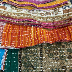 Op de afbeelding: Een stapel kleurrijke kantha-dekens met ingewikkelde patronen en stiksels. De dekens zijn gemaakt van gerecyclede sari's en zijn een traditioneel Indiaas ambacht.