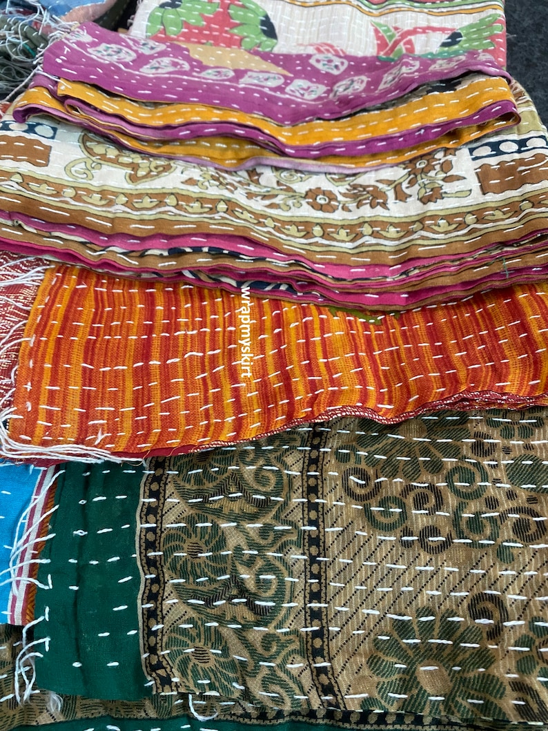 Op de afbeelding: Een stapel kleurrijke kantha-dekens met ingewikkelde patronen en stiksels. De dekens zijn gemaakt van gerecyclede sari's en zijn een traditioneel Indiaas ambacht.