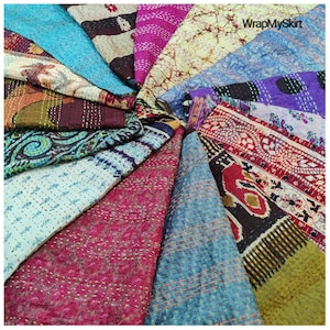 May include: A collection of colorful kantha quilts arranged in a circular pattern. The quilts are made of recycled saris and feature intricate embroidery and patchwork designs. The quilts are a vibrant mix of colors, including blue, green, red, purple, and brown.