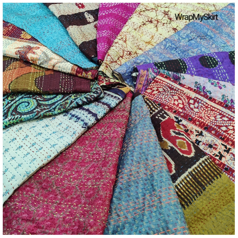 May include: A collection of colorful kantha quilts arranged in a circular pattern. The quilts are made of recycled saris and feature intricate embroidery and patchwork designs. The quilts are a vibrant mix of colors, including blue, green, red, purple, and brown.