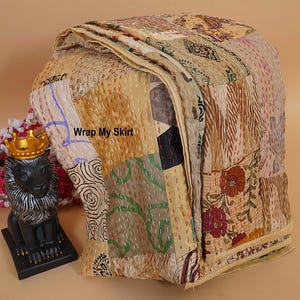 Könnte beinhalten: Eine gefaltete Patchwork-Decke mit verschiedenen beigen, braunen und ockerfarbenen Stoffquadraten mit Blumen- und geometrischen Mustern, akzentuiert durch sichtbare Steppstiche. Der Text Wrap My Skirt ist auf den Stoff gedruckt.