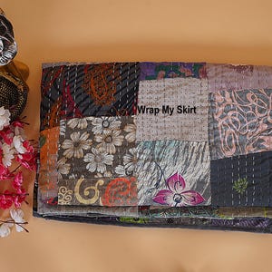 Könnte beinhalten: Ein gefaltetes Patchwork-Textil mit verschiedenen gemusterten Stoffen in Grau-, Braun-, Lila- und Orangetönen. Das Textil weist florale und abstrakte Designs mit sichtbaren Nähten auf. Der Text "Wrap My Skirt" ist sichtbar.