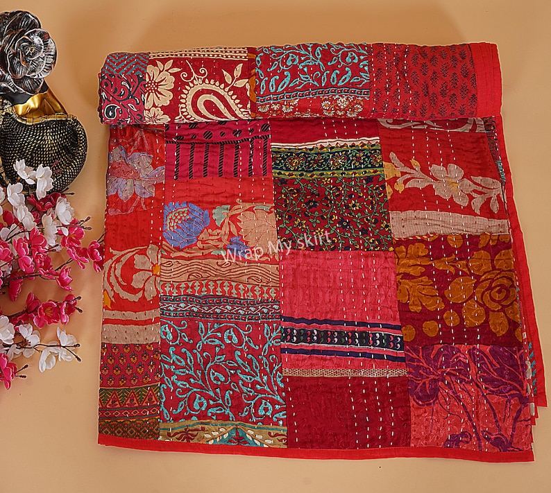 May include: A red and gold patchwork quilt with a variety of floral and paisley patterns. The quilt is made of kantha stitching and is a traditional Indian craft.