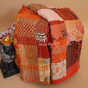 Pu&ograve; includere: Un quilt patchwork realizzato con diversi tessuti in tonalit&agrave; di arancione, marrone e bianco. Il quilt &egrave; piegato e presenta un design cucito. Il testo "Wrap My Skirt" &egrave; visibile sul quilt.