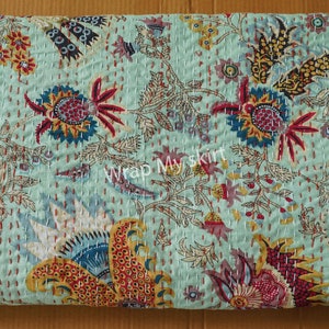 May include: A turquoise blue kantha quilt with a floral pattern in shades of red, yellow, and blue. The quilt is hand-stitched and has a traditional Indian design. "Wrap My Skirt" is printed in the center of the quilt.