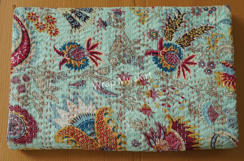 May include: A turquoise blue kantha quilt with a floral pattern in shades of red, yellow, and blue. The quilt is hand-stitched and has a traditional Indian design. "Wrap My Skirt" is printed in the center of the quilt.