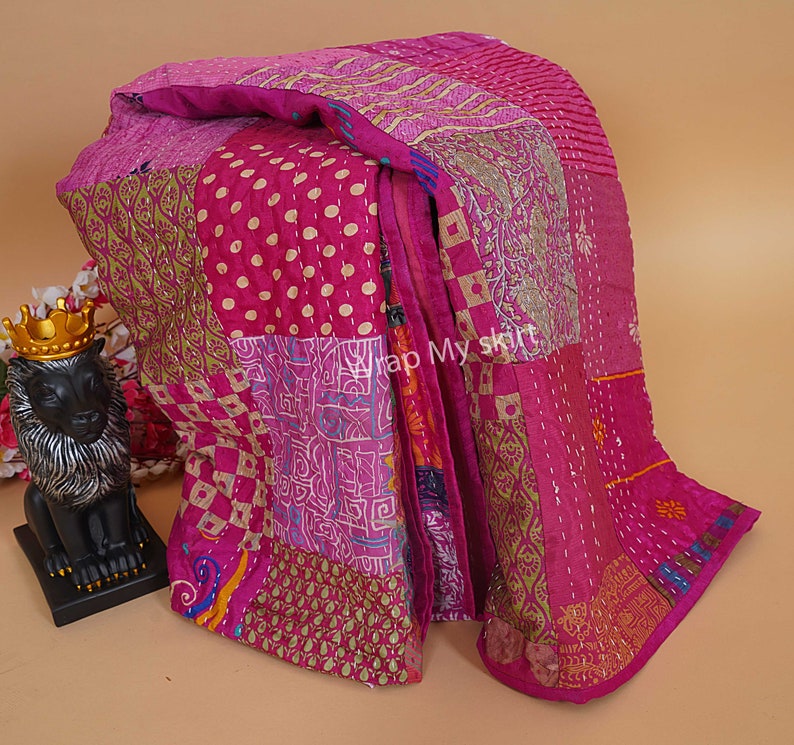Puede incluir: Una colcha kantha rosa y dorada con un dise&ntilde;o de patchwork. La colcha est&aacute; hecha de saris reciclados y tiene una variedad de patrones, incluyendo lunares, paisley y dise&ntilde;os florales.