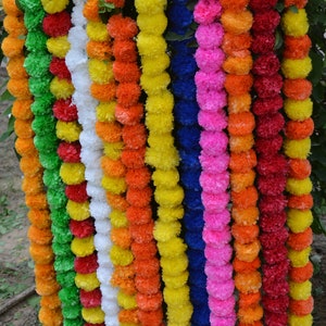 May include: A colourful garland of artificial marigold flowers, with each strand in a different colour, including green, white, yellow, orange, red, blue, and pink.