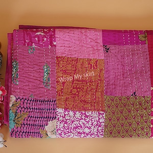 Könnte beinhalten: Eine rosafarbene und grüne Patchwork-Decke mit verschiedenen Mustern. Die Decke besteht aus verschiedenen Stoffen und hat eine handgenähte Optik. Der Text "Wrap My Skirt" ist in der Mitte der Decke sichtbar.