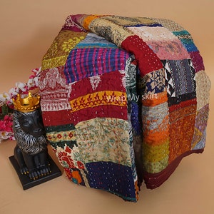 Könnte beinhalten: Eine farbenfrohe Patchwork-Decke aus recycelten Saris. Die Decke besteht aus Quadraten aus verschiedenen Stoffen, Farben und Mustern. Die Decke ist zur Hälfte gefaltet und liegt auf einer hellbraunen Oberfläche.