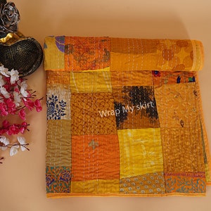 May include: A yellow and orange patchwork quilt with a variety of patterns and textures. The quilt is made of recycled saris and is hand-stitched. The quilt is rolled up and has a tag that says "Wrap My Skirt".
