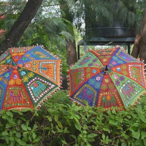 Könnte beinhalten: Zwei farbenfrohe, dekorative Sonnenschirme mit aufwendigen Stickmustern. Die Sonnenschirme zeigen eine lebendige Mischung aus Rot, Blau, Orange und Grün, mit Elefanten- und Blumenmotiven. Jeder Schirm ist mit Fransen verziert.