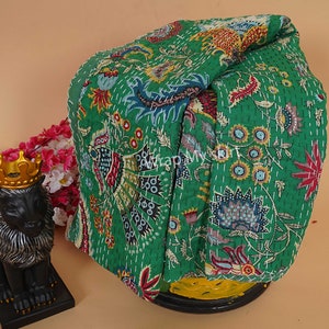 May include: A green kantha quilt with a floral pattern. The quilt is folded and displayed on a yellow surface.