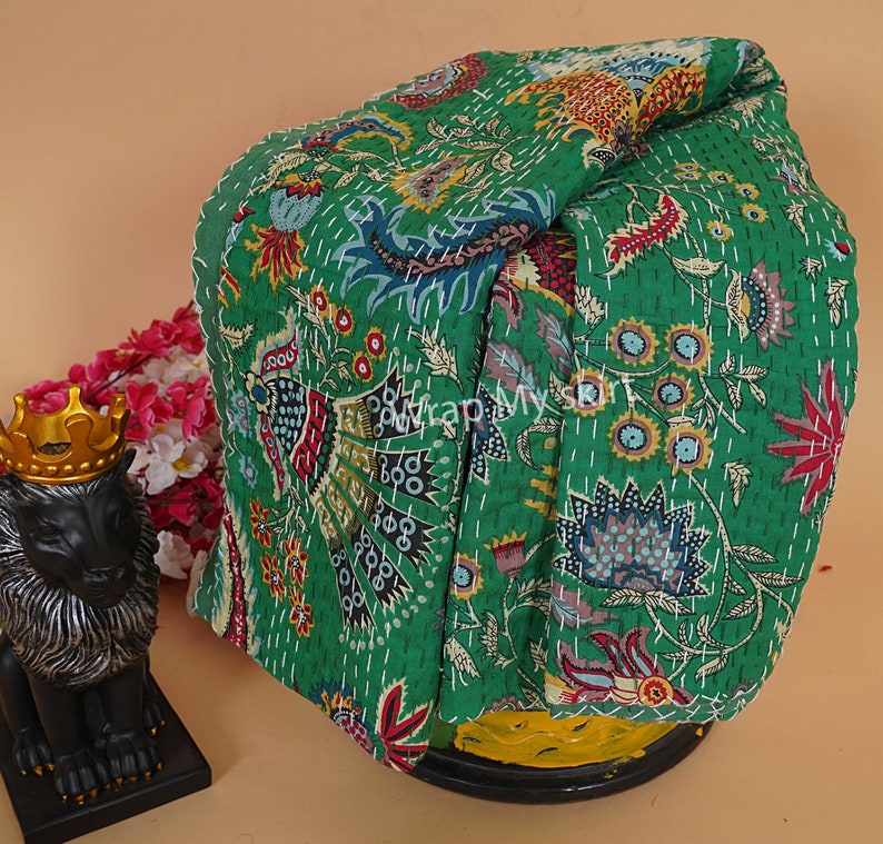 May include: A green kantha quilt with a floral pattern. The quilt is folded and displayed on a yellow surface.
