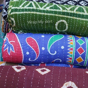 May include: A stack of four kantha quilts in various colours and patterns. The top quilt is orange with a floral design, the second is green with a geometric design, the third is blue with a paisley design, and the bottom quilt is brown with a diamond pattern. The quilts are all hand-stitched and have a vintage look.