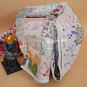 Pu&ograve; includere: Un quilt bianco a patchwork con una variet&agrave; di motivi floreali e colori. Il quilt &egrave; piegato a met&agrave; e ha un bordo bianco. Il testo "Wrap My Skirt" &egrave; visibile sul quilt.