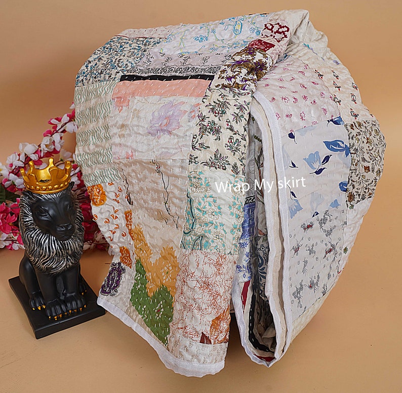 Pu&ograve; includere: Un quilt bianco a patchwork con una variet&agrave; di motivi floreali e colori. Il quilt &egrave; piegato a met&agrave; e ha un bordo bianco. Il testo "Wrap My Skirt" &egrave; visibile sul quilt.