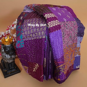 Könnte beinhalten: Eine gefaltete Patchwork-Steppdecke in verschiedenen Lilatönen. Die Decke weist eine Vielzahl von Stoffmustern und -strukturen mit sichtbaren Nähten auf. Der Text "Wrap My Skirt" ist auf der Steppdecke zu sehen.