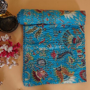 May include: A turquoise blue kantha quilt with a floral and paisley pattern. The quilt is hand-stitched and has a soft, textured surface.